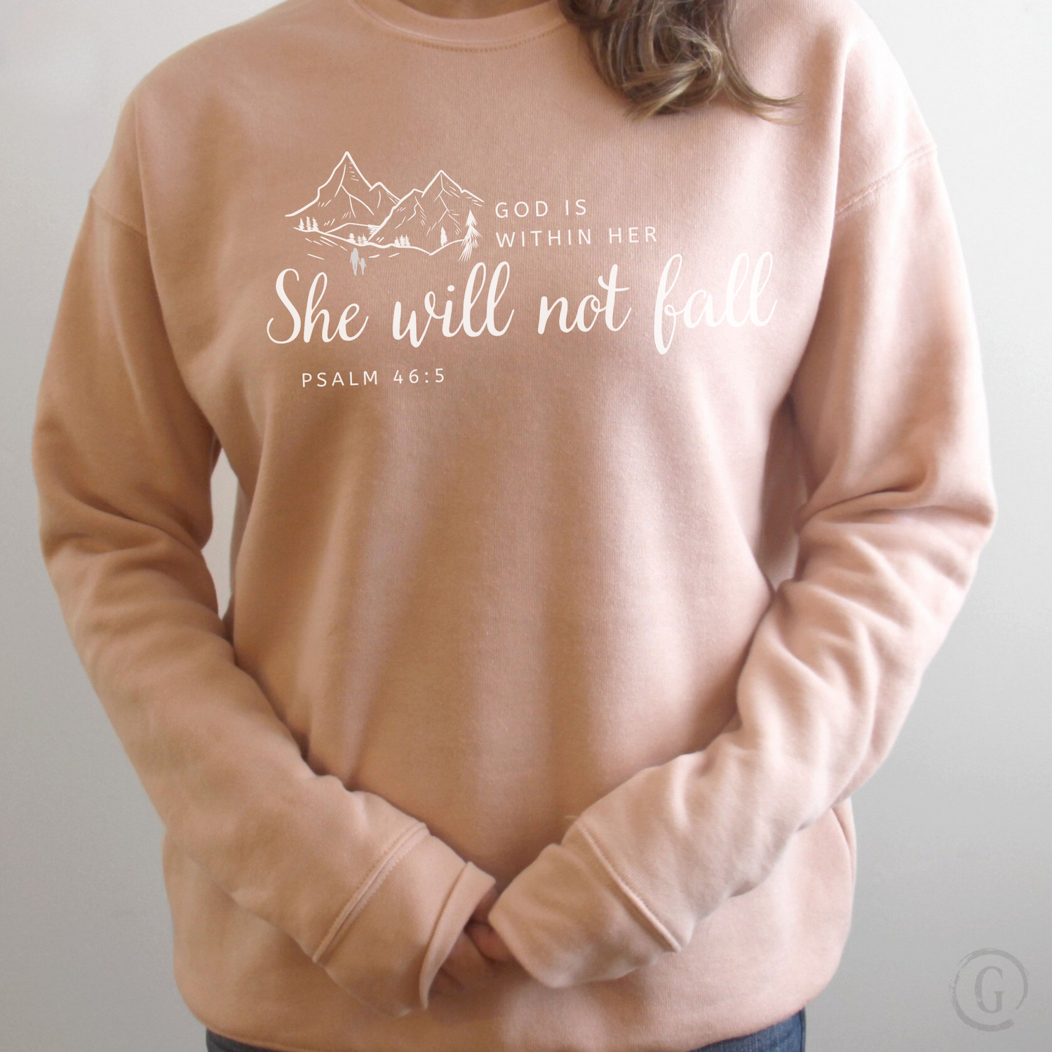 A person wearing a white sweatshirt with a mountain-themed design and the text &