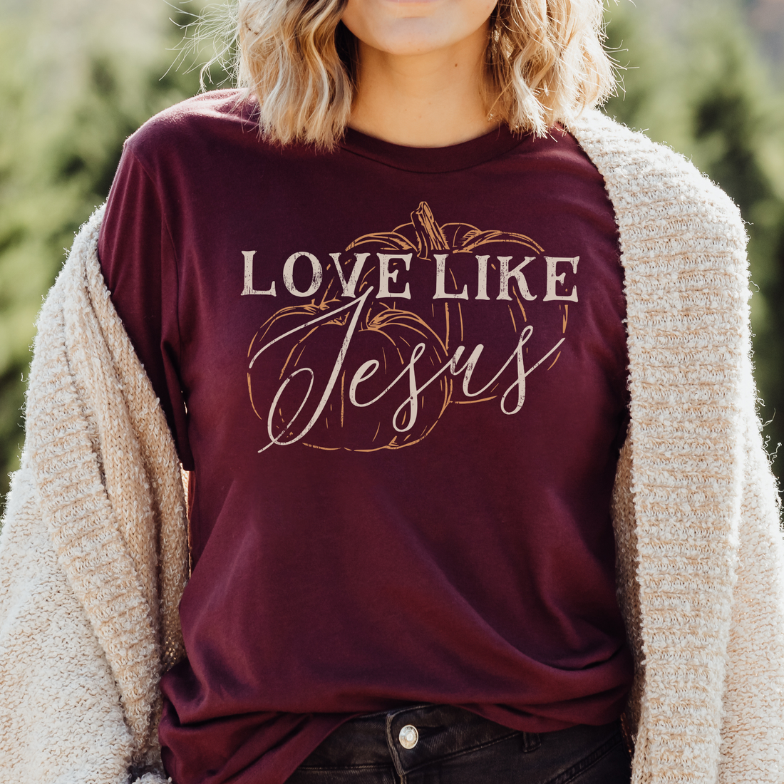 Person wearing a maroon shirt with 'Love Like Jesus' text and pumpkin design outdoors.